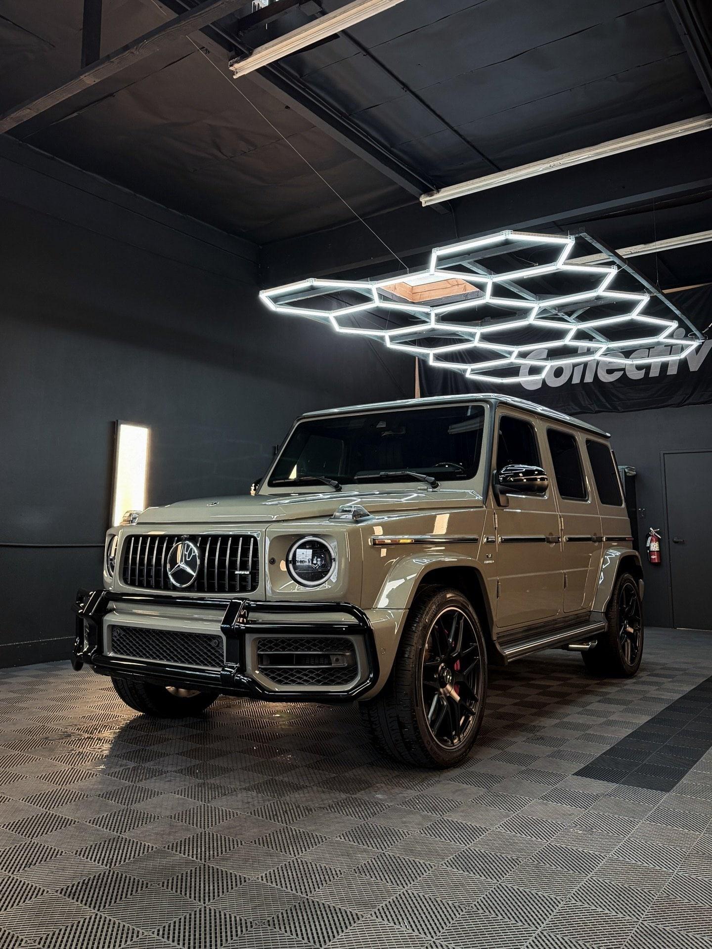 Sand-colored Mercedes-AMG G63 under hexagon lights and the Collective banner