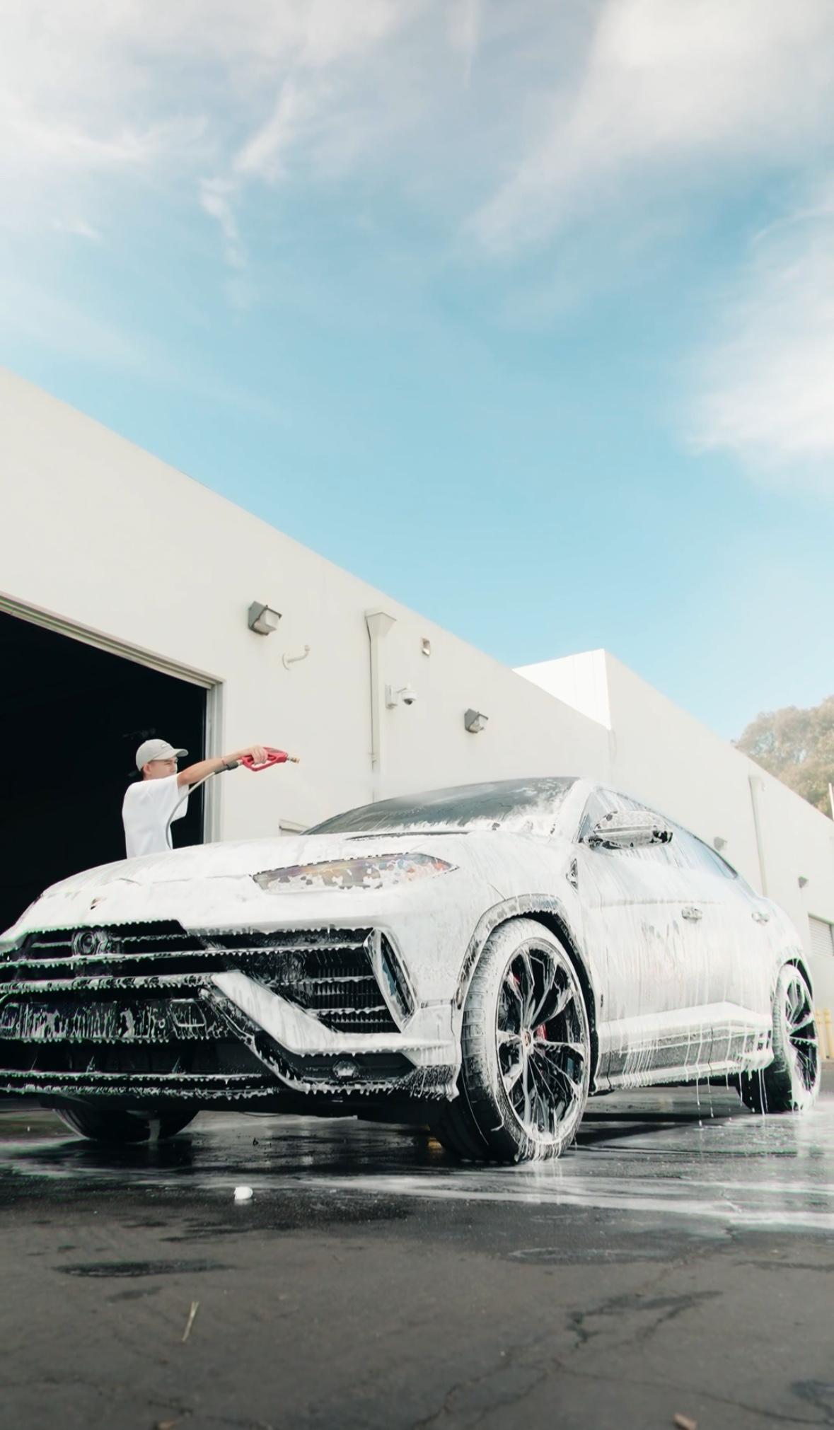 Detailer foam washing a white Lamborghini Urus outside the Irvine studio